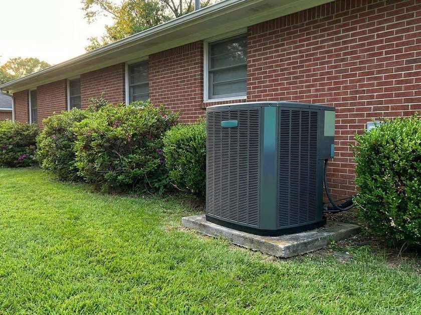 Heat pump outdoor unit on a concrete pad beside a brick ranch house, the kind of install Georgia heat pump rebates help pay for